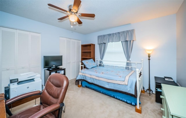 bedroom with ceiling fan, two closets, and light colored carpet