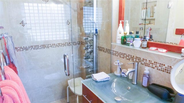 bathroom with a shower with shower door, tile walls, decorative backsplash, and vanity