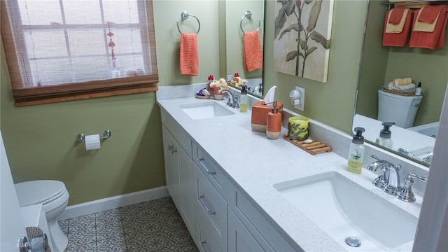 full bath featuring toilet, double vanity, baseboards, and a sink