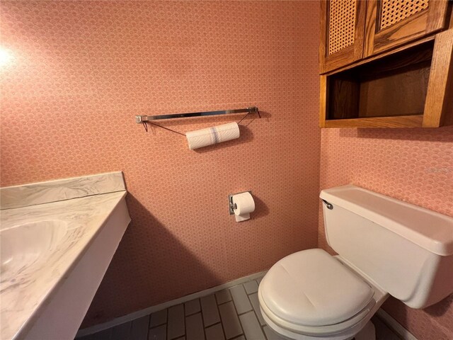 half bath with baseboards, toilet, and wallpapered walls