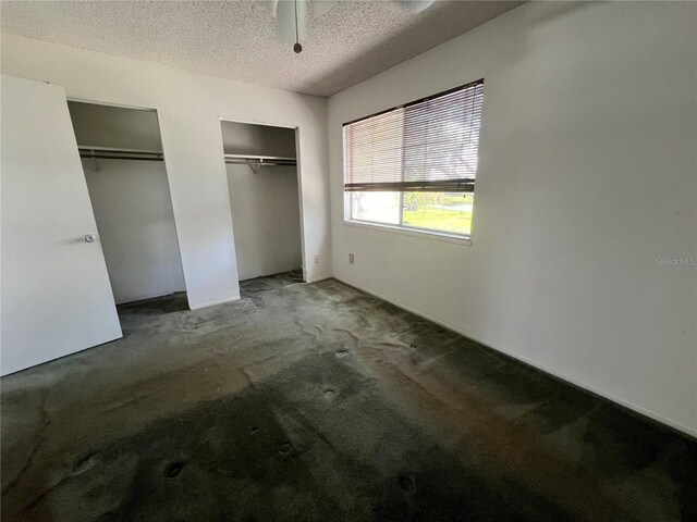 unfurnished bedroom with a textured ceiling, carpet flooring, and multiple closets