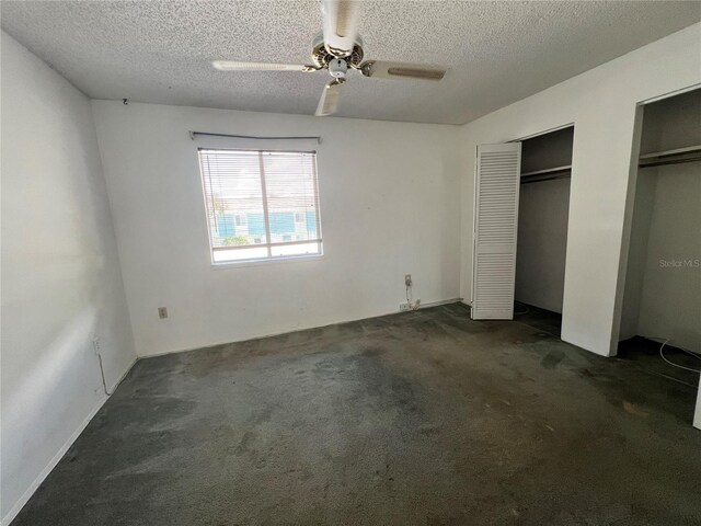 unfurnished bedroom with ceiling fan, dark carpet, a textured ceiling, and two closets