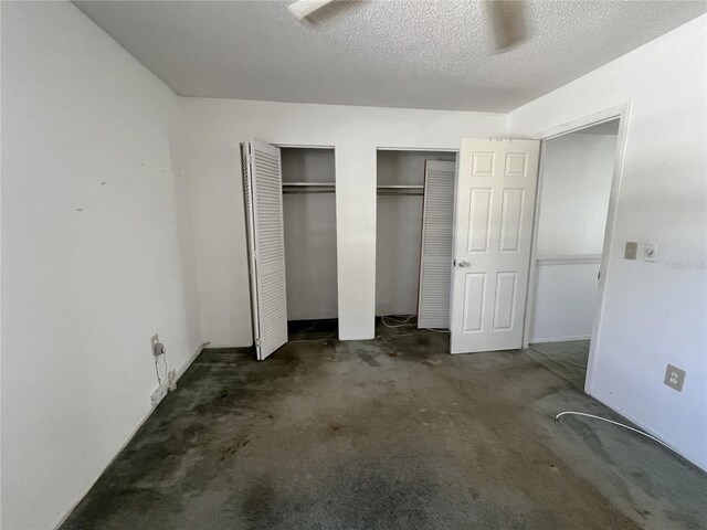 unfurnished bedroom featuring a textured ceiling, dark colored carpet, and two closets