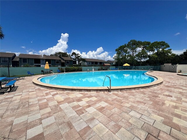 community pool with a patio area, fence, and a residential view