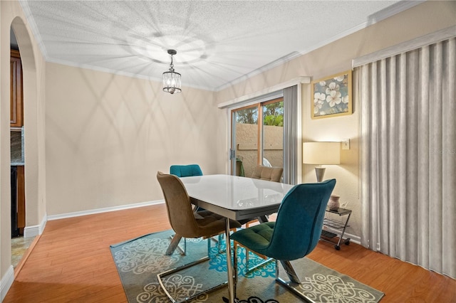 dining space with a textured ceiling, arched walkways, wood finished floors, baseboards, and crown molding