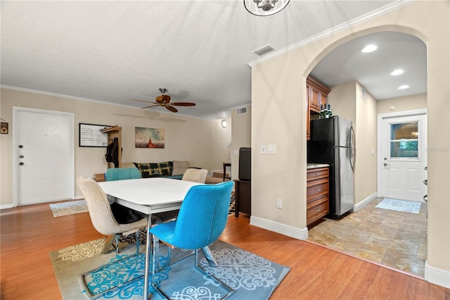 dining space featuring arched walkways, visible vents, crown molding, and light wood-style flooring