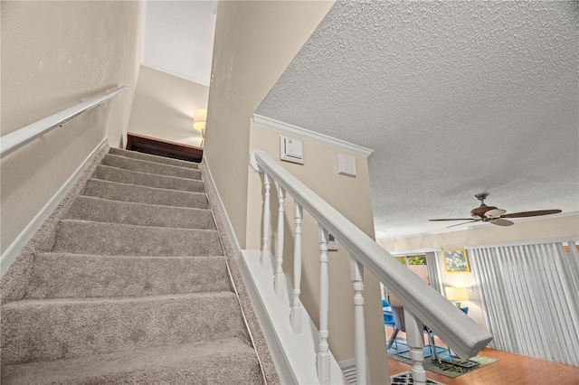 staircase with a textured ceiling, ceiling fan, baseboards, and crown molding