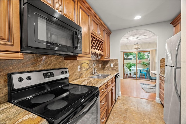 kitchen featuring brown cabinets, stainless steel appliances, tasteful backsplash, a sink, and light stone countertops