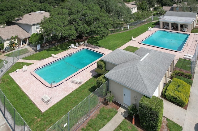 community pool with an outbuilding, a lawn, a patio area, fence, and a storage structure