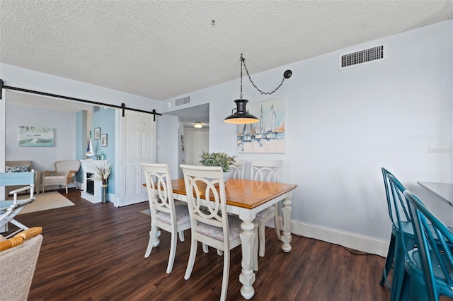 dining room with a textured ceiling, a barn door, and dark hardwood / wood-style floors