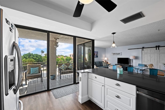 kitchen with a barn door, stainless steel appliances, white cabinetry, dark wood-type flooring, and ceiling fan