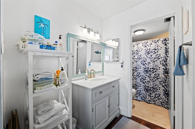 bathroom with toilet, a shower with curtain, wood-type flooring, vanity, and a textured ceiling