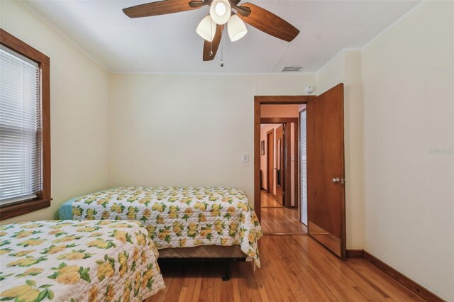 bedroom featuring multiple windows, light hardwood / wood-style flooring, ceiling fan, and ornamental molding