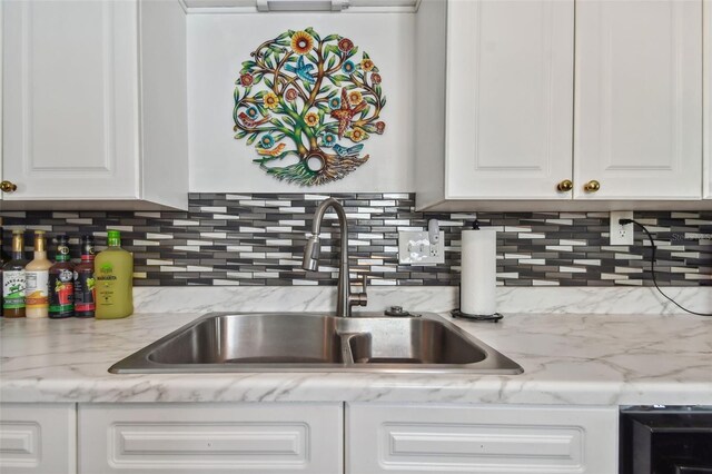 kitchen featuring white cabinets, backsplash, light stone counters, and sink