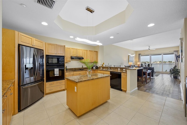 kitchen with a raised ceiling, black appliances, a center island, and light stone countertops