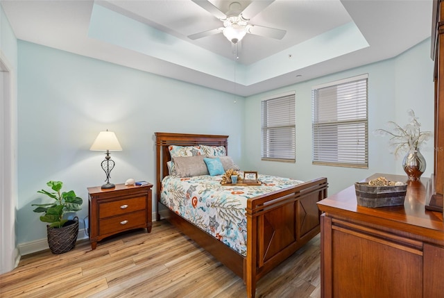 bedroom with ceiling fan, a raised ceiling, and light hardwood / wood-style floors