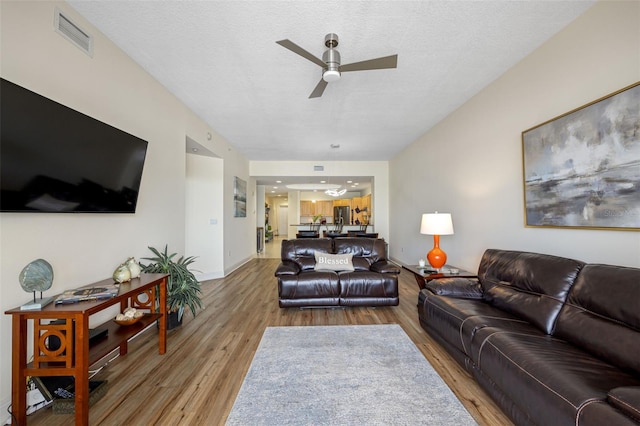 living room featuring ceiling fan, light hardwood / wood-style floors, and a textured ceiling