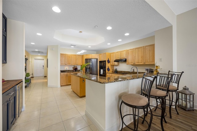 kitchen with dark stone counters, a raised ceiling, a kitchen breakfast bar, oven, and stainless steel refrigerator with ice dispenser