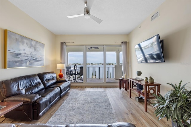 living room with light wood-type flooring, ceiling fan, and a textured ceiling