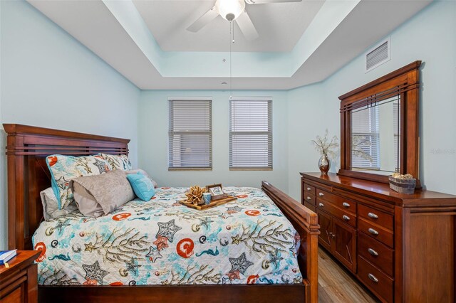 bedroom featuring light hardwood / wood-style flooring, ceiling fan, and a raised ceiling