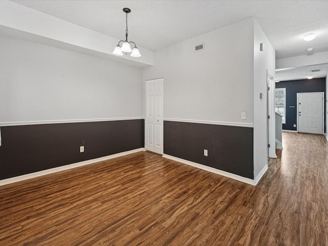 empty room with a notable chandelier, a textured ceiling, and hardwood / wood-style floors