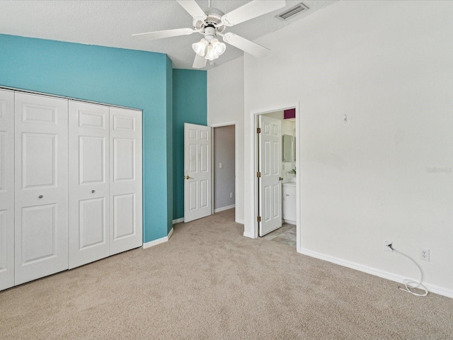 unfurnished bedroom featuring high vaulted ceiling, a closet, ensuite bathroom, light carpet, and ceiling fan