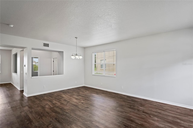 spare room with a textured ceiling, dark hardwood / wood-style floors, and a chandelier