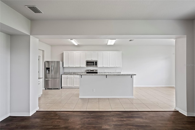 kitchen with stainless steel appliances, white cabinetry, and light hardwood / wood-style floors