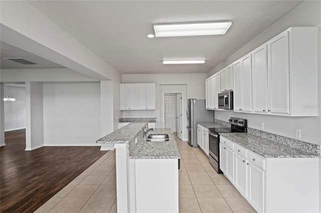 kitchen with light hardwood / wood-style flooring, appliances with stainless steel finishes, white cabinetry, sink, and an island with sink