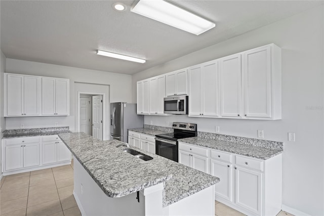 kitchen with an island with sink, stainless steel appliances, light stone countertops, and white cabinetry