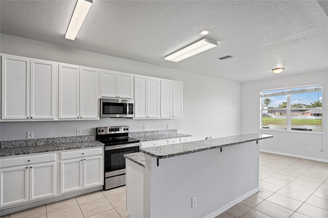 kitchen with dark stone counters, appliances with stainless steel finishes, light tile patterned floors, and white cabinets