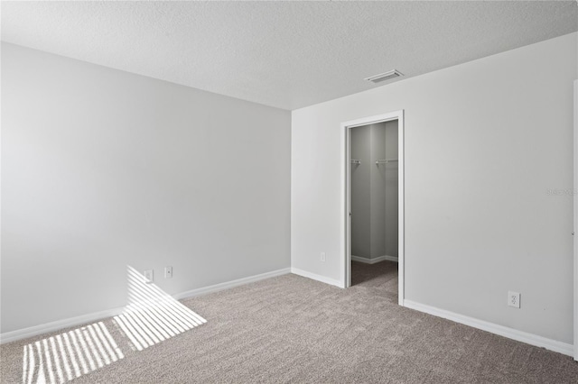 unfurnished bedroom with light carpet, a textured ceiling, a walk in closet, and a closet