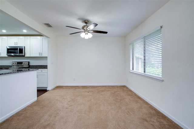 kitchen featuring ceiling fan, dark stone countertops, carpet floors, white cabinets, and appliances with stainless steel finishes