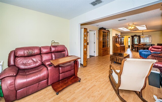 living room with ceiling fan, light hardwood / wood-style floors, and a textured ceiling