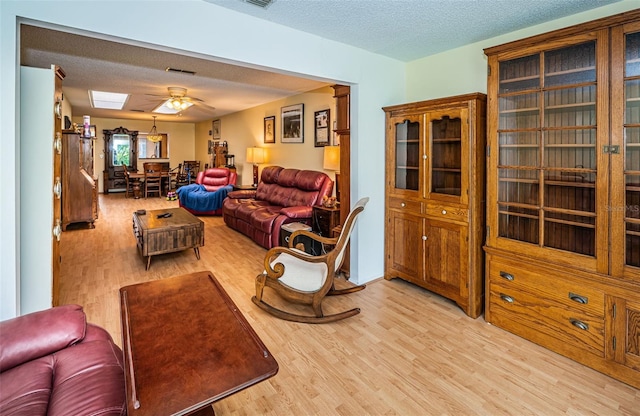 living room with ceiling fan, a textured ceiling, and light hardwood / wood-style flooring