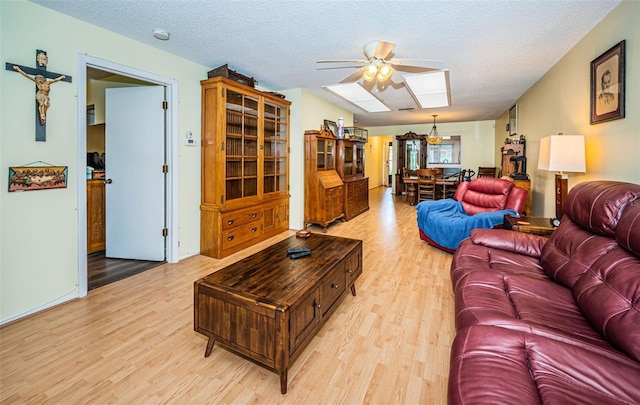 living room with a textured ceiling, light hardwood / wood-style flooring, ceiling fan, and a skylight