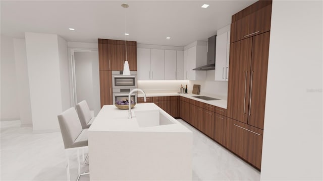 kitchen featuring wall chimney range hood, black electric stovetop, a breakfast bar, sink, and a center island with sink