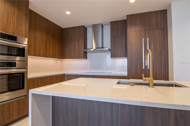 kitchen with light stone counters, stainless steel double oven, black electric cooktop, wall chimney range hood, and modern cabinets