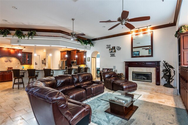 living room featuring crown molding, ceiling fan, and a tiled fireplace