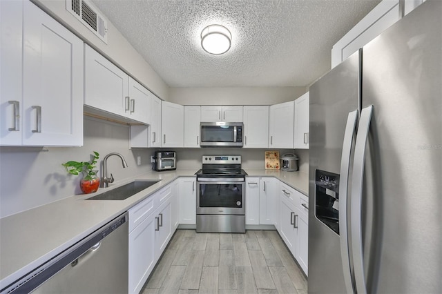 kitchen featuring light wood-type flooring, white cabinetry, stainless steel appliances, and sink