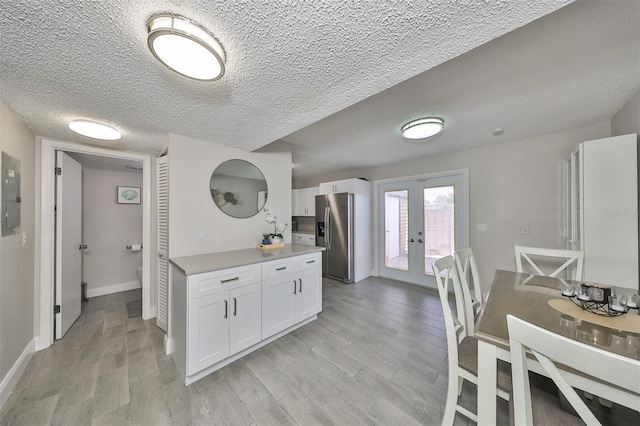 kitchen with a textured ceiling, stainless steel fridge, french doors, light wood-type flooring, and white cabinets