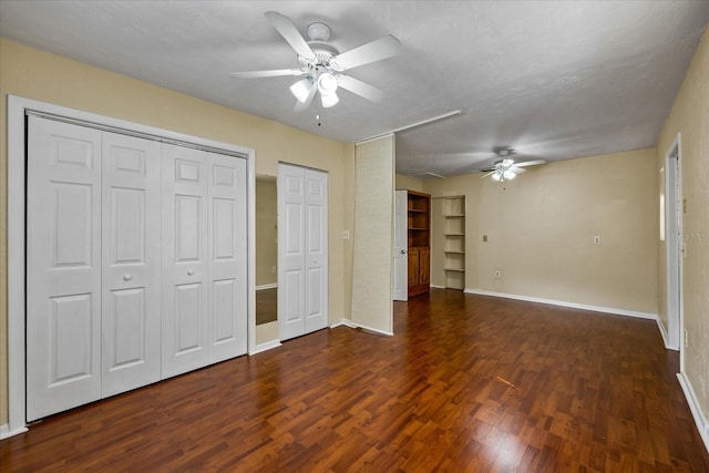 unfurnished bedroom with two closets, a textured ceiling, dark hardwood / wood-style floors, and ceiling fan