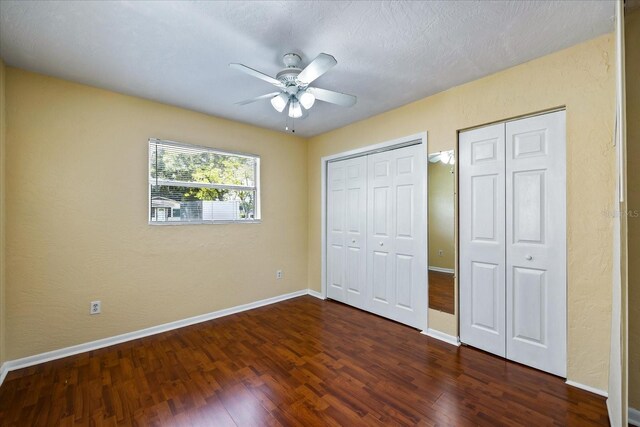 unfurnished bedroom with a textured ceiling, two closets, ceiling fan, and dark hardwood / wood-style floors