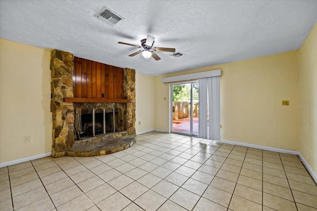 unfurnished living room featuring ceiling fan, a stone fireplace, light tile patterned floors, and a textured ceiling