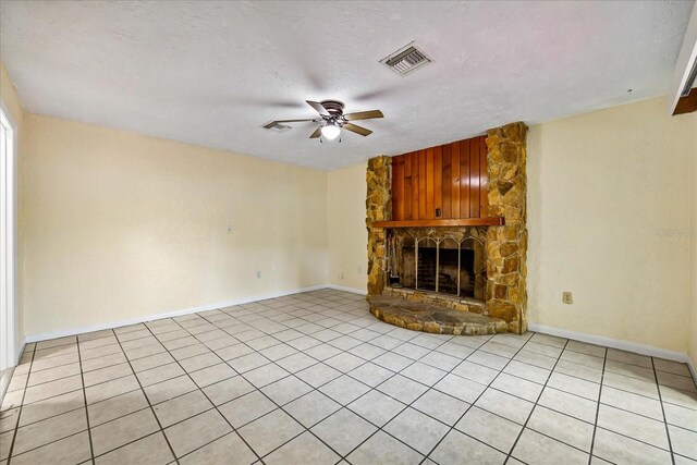 unfurnished living room featuring ceiling fan, light tile patterned flooring, a stone fireplace, and a textured ceiling