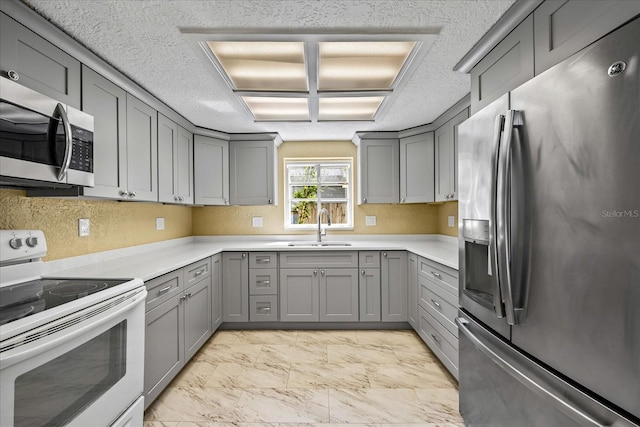 kitchen with gray cabinetry, sink, stainless steel appliances, and a textured ceiling