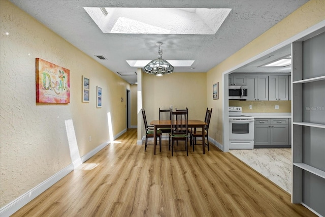 dining room with a chandelier, light wood-type flooring, a textured ceiling, and a skylight