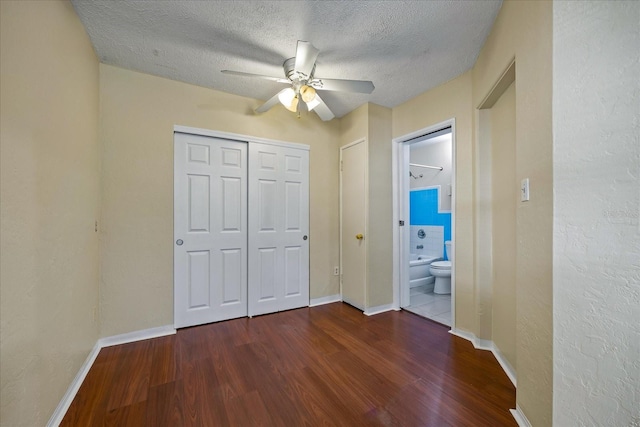 unfurnished bedroom featuring a textured ceiling, ceiling fan, dark wood-type flooring, and connected bathroom