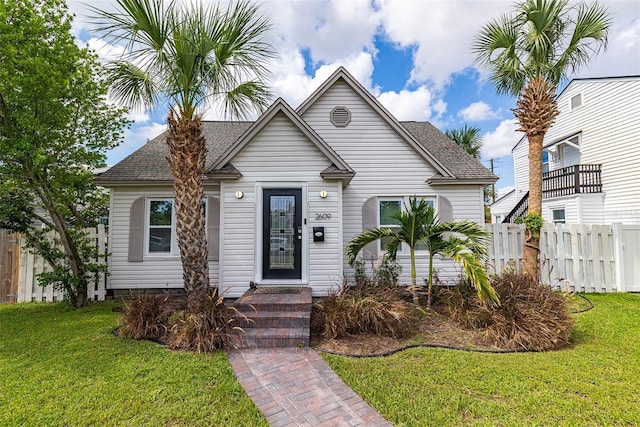 bungalow with a shingled roof, fence, and a front yard