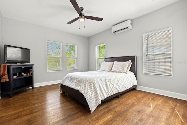 bedroom with a ceiling fan, a wall unit AC, baseboards, and wood finished floors